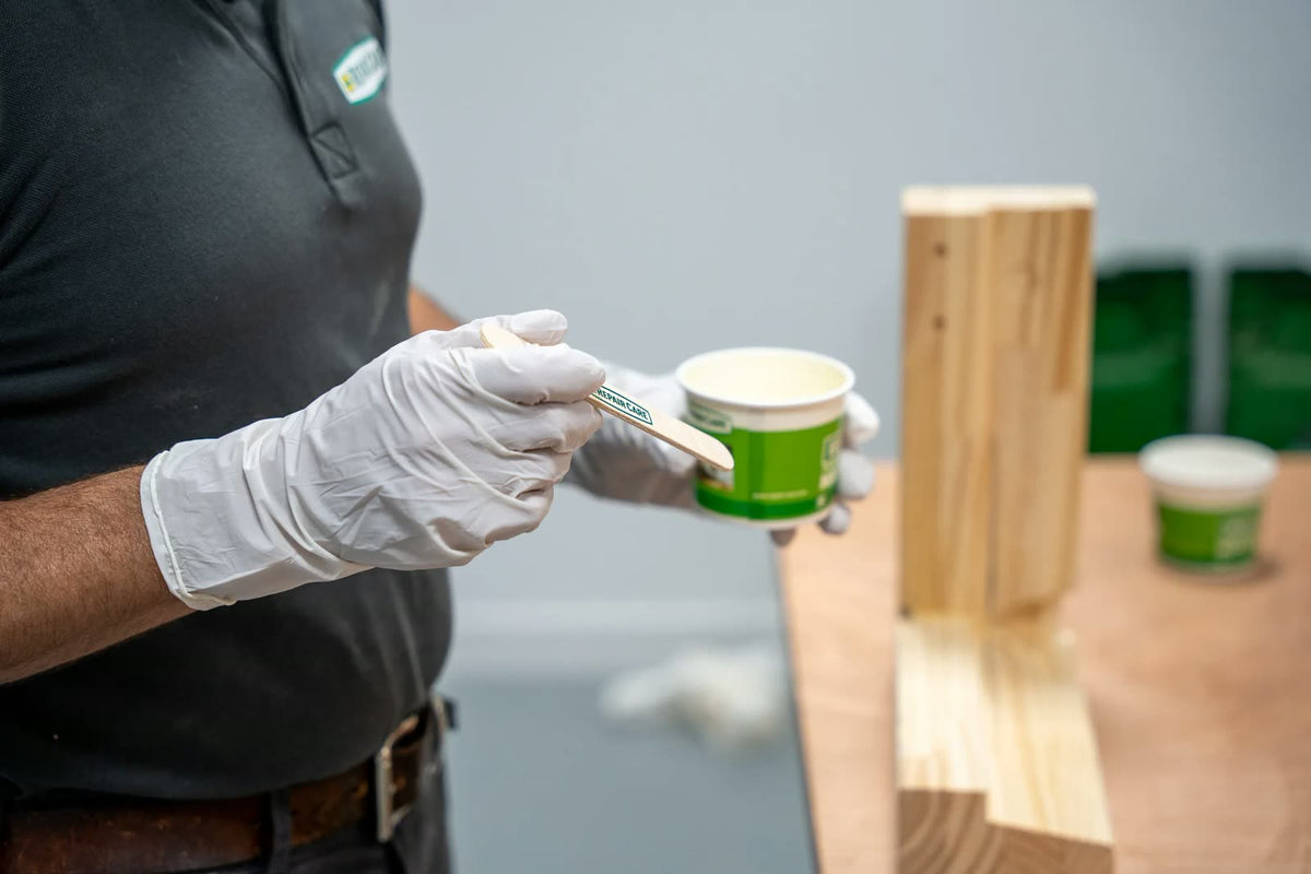 Gloved hand mixing filler next to a wooden post, wearing EASY Q nitrile gloves